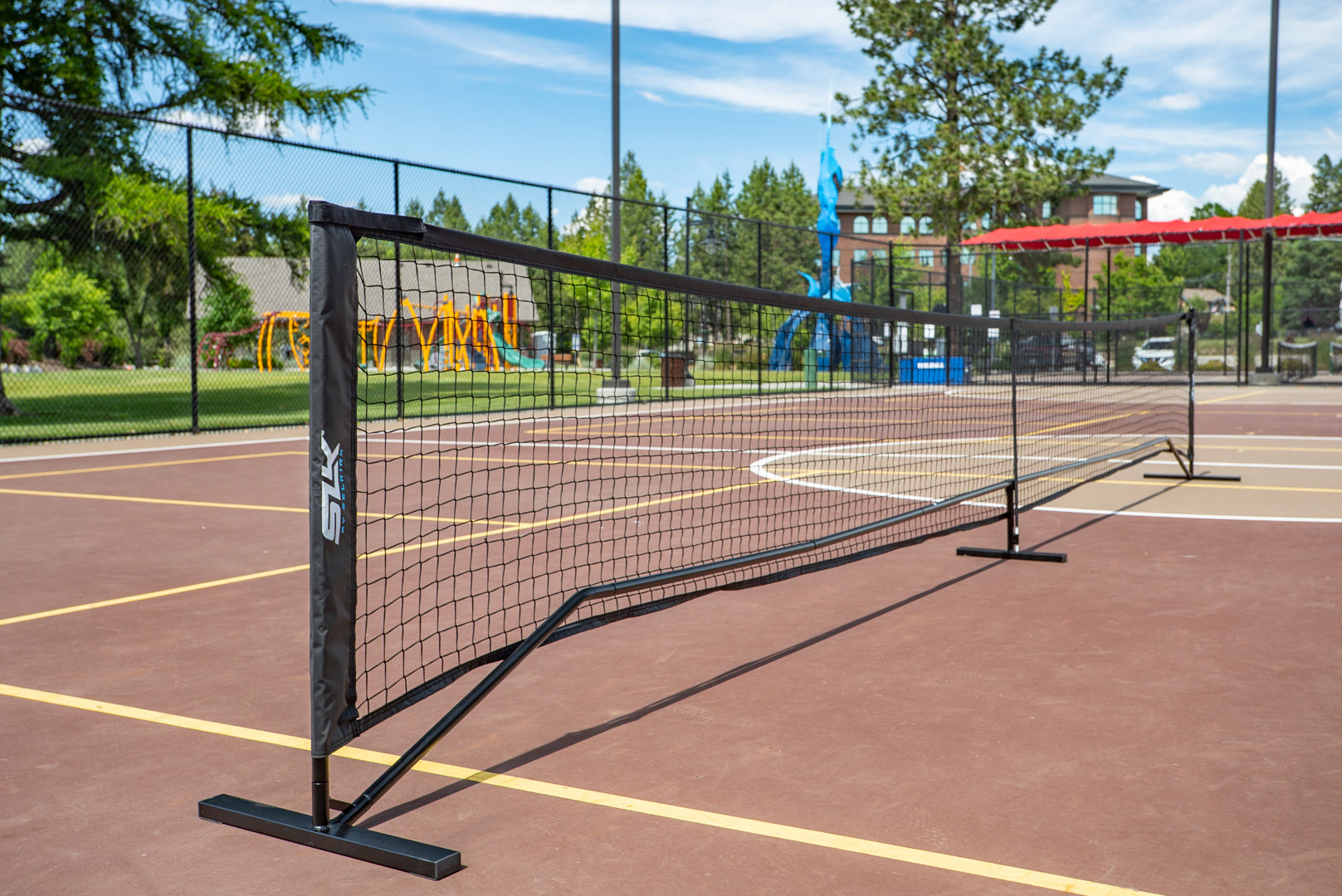Selkirk SLK Pro Portable Pickleball Net set up on a court with playground equipment in the background.